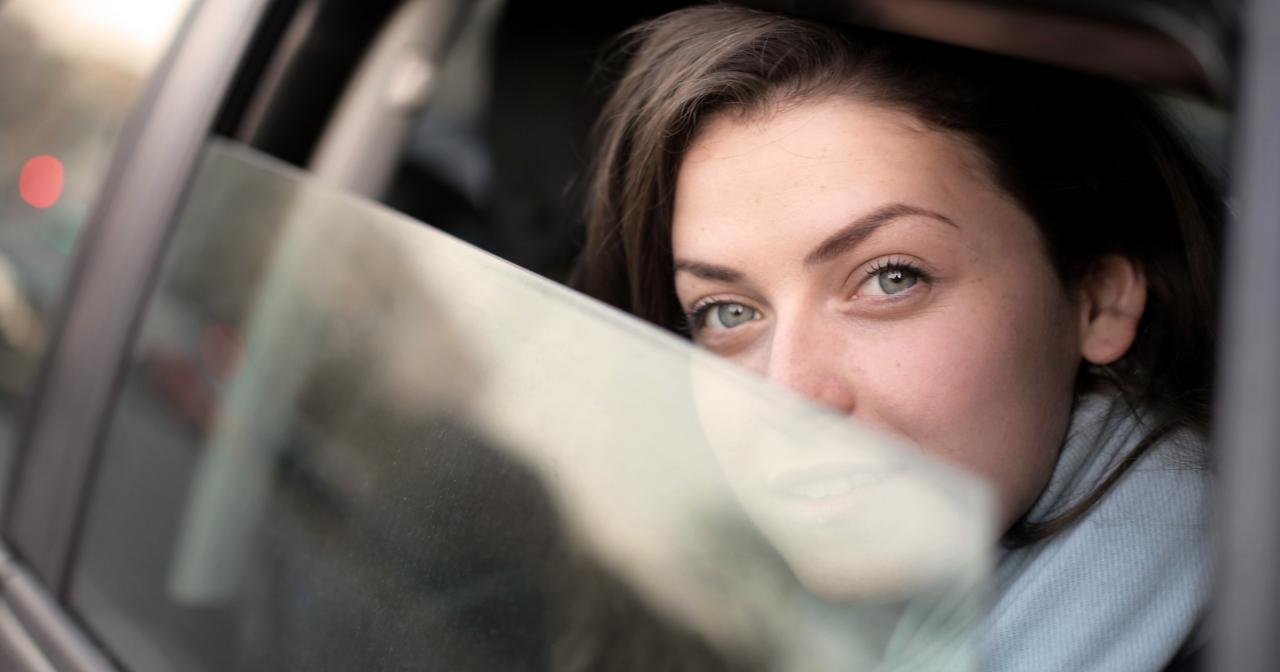 Frau ohne Brille schaut aus einem halb geöffneten Autofenster
